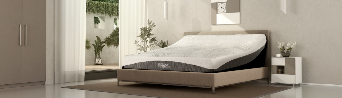 White and gray smooth top mattress with American Mattress logo, set up in a luxurious tan bedroom on an adjustable base